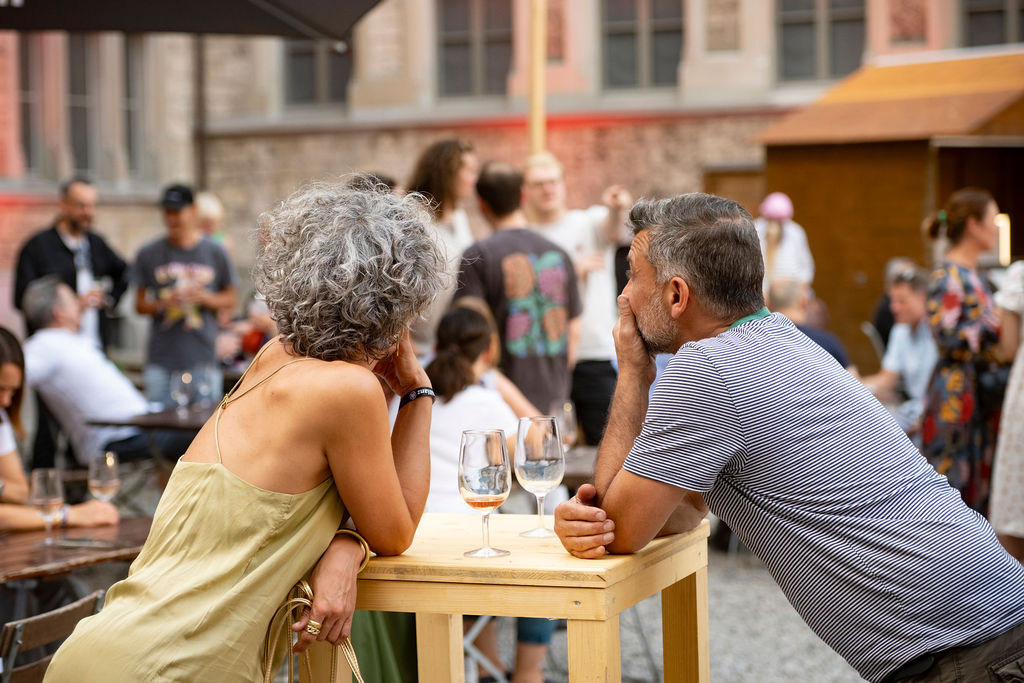 Gäste geniessen einen entspannten Abend mit Wein beim Hofkino Zürich – gesellige Stimmung im Innenhof des Landesmuseums